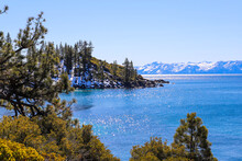 A Stunning Shot Of The Vast Clear Blue Lake Water With Snow Capped Mountains And Lush Green Trees Along The Banks Of The Lake And Blue Sky At Lake Tahoe Nevada State Park In Incline Village Nevada