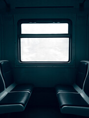 Dark empty cabin of a passenger train car with seats and a window in the center behind which is a white sky.