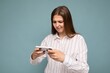 © Ivan Traimak - Concentrated attractive young blonde woman wearing casual white shirt isolated over blue background wall holding smartphone and playing online games looking at gadjet screen