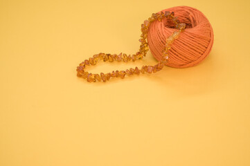 Sticker - Closeup shot of an amber beads necklace and a cotton yarn on a yellow surface