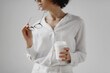 © Olena Bloshchynska - Cropped image of young woman holding eyeglasses and drinking coffee from paper cup over white background.