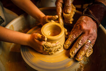 A Close-up Of The Hand Of A Male Potter Who Teaches His Pupil, A Child Of The Art Of Making A Pot Or A Vase Of Clay. People Working On Potters.