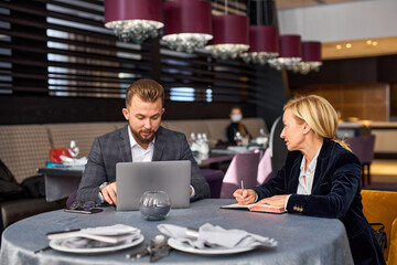 Wall Mural - two business partners discussing project using laptop, theysit in restaurant talking, co-working