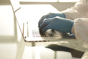 Doctor in blue gloves typing on a laptop in a hospital room