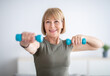 © Prostock-studio - Portrait of positive senior lady exercising with dumbbells at home during covid-19 quarantine