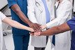 © Roman - Cropped Multi-ethnic professional doctors men women teamwork coordinate hands fighting covid-19 virus, healthy volunteer doctors team holding hands together