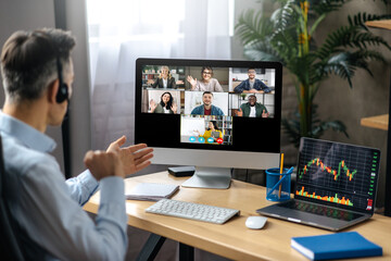 Online lesson or business webinar. Successful man sits at the work desk, on a computer screen are different multiracial people and teacher gathered in an online lecture by video conference