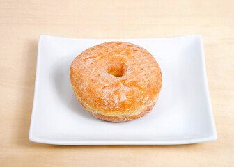 Wall Mural - One round sugar coated donut on a rectangular porcelain plate on a light wood table.