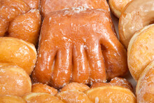Close Up On Variety Of Donuts Arranged On Parchment Paper Clustered Together. Bear Claw In The Center Surrounded By Glazed Twists, Cinnamon Twist, Jelly Filled, Sugar Coated, Coconut Covered.