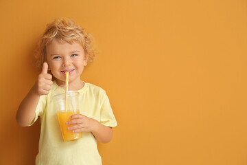 Cute little boy drinking orange juice on color background