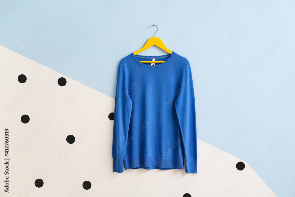 Hanger with stylish sweater on color background