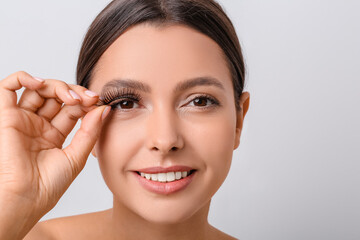 Sticker - Beautiful young woman applying fake eyelashes against light background