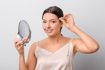 Canvas Print - Beautiful young woman applying fake eyelashes against light background