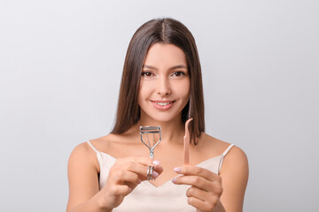 Canvas Print - Beautiful young woman with eyelash curler and tweezers on light background