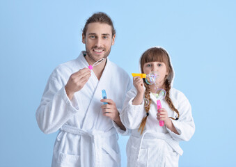 Sticker - Happy father and daughter in bathrobes blowing soap bubbles on color background