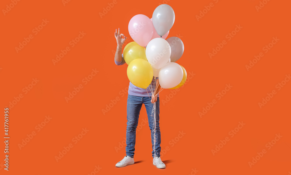 Handsome young man with balloons showing OK on color background