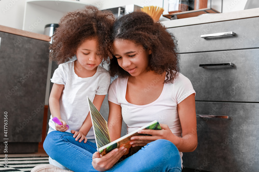 Cute African-American sisters reading book at home