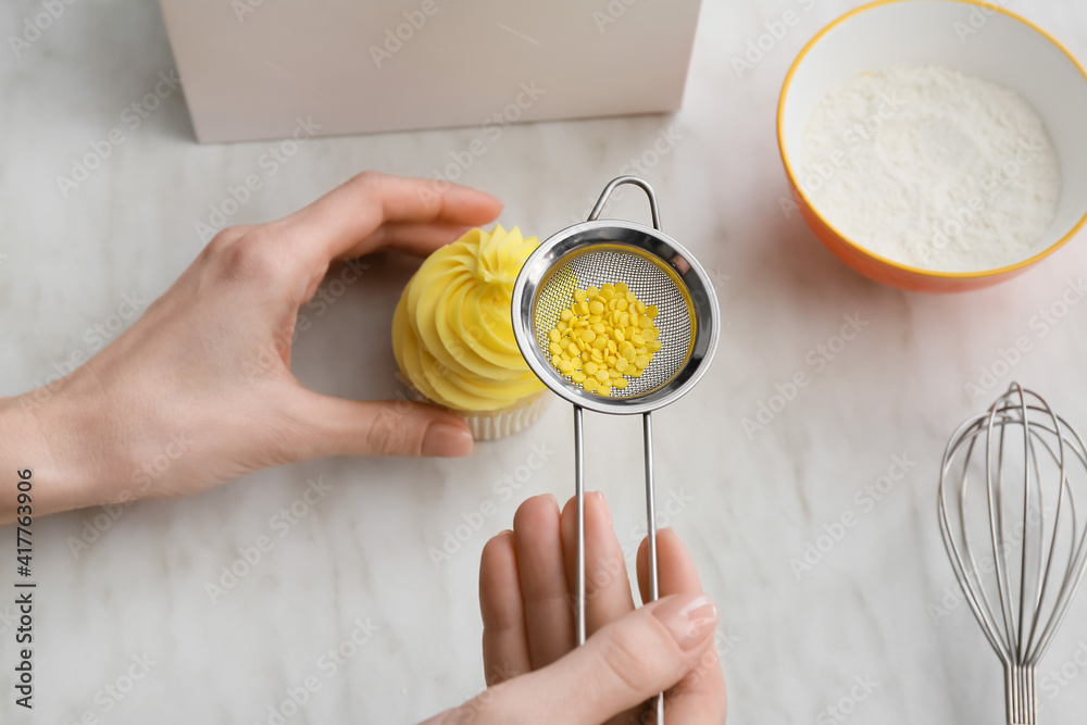 Woman decorating tasty cupcake on table