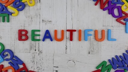 Fototapete - Colorful alphabet letters spelling the word - Beautiful - on a grey wooden background with corner decoration of further letters viewed from overhead. Stop motion, top view