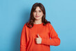 Image of beautiful brunette woman wearing casual clothes showing thumbs up and looking directly at camera at camera with cute charming smile, posing isolated over blue wall.