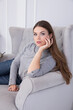 © Fotostudijas.lv - A beautiful brunette sits on a grey sofa.
