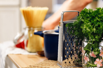 Close up of kitchen table with grater, cooking pot and raw spaghetti