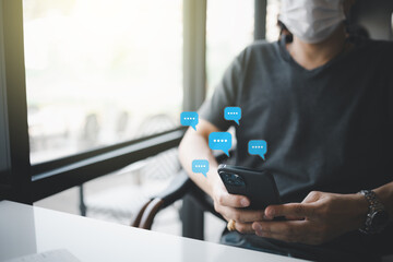 Wall Mural - closeup man wearing face mask hand holding smartphone with message icon as chatting in cafe