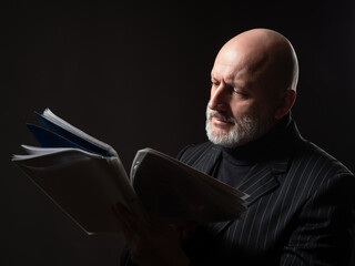 Wall Mural - Businessman over black background. Man with a beard is holding papers. He flips through some documentation. Concept is experienced businessman. Experienced company manager. Portrait of adult manager