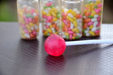 Canvas Print - Pink lollypop with sweet anise beans colorful plastic bottle on the brown background.