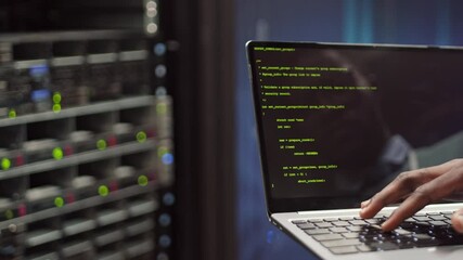 Wall Mural - back view of unrecognizable male programmer coding on laptop while standing in modern data center