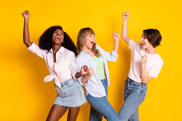 Wall Mural - Portrait of three attractive cheerful girls dancing having fun clubbing isolated over bright yellow color background
