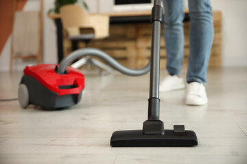 Canvas Print - Young man using vacuum cleaner at home, closeup