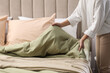 © New Africa - Woman making bed with new pistachio linen in room, closeup