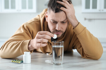 Wall Mural - Man taking medicine for hangover at table in kitchen