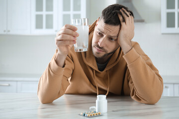 Wall Mural - Man taking medicine for hangover at table in kitchen