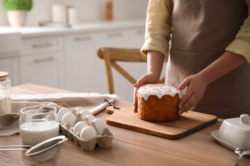 Wall Mural - Young woman with traditional Easter cake at table in kitchen, closeup