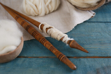 Wall Mural - Soft white wool and spindles on blue wooden table, closeup