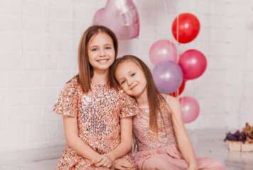 Two girls in fancy dresses in a light studio with balloons