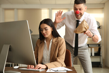 Man popping paper bag behind his colleague in office. Funny joke