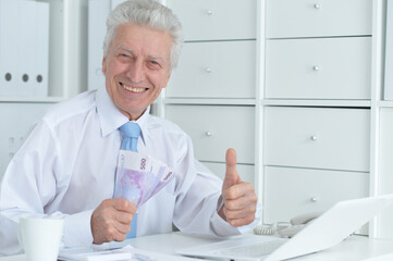 Senior doctor sitting at table with laptop and holding money