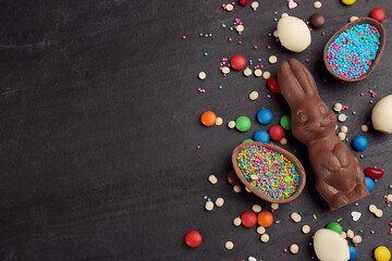 Flat lay composition with chocolate Easter bunny, eggs and candies on black table. Space for text