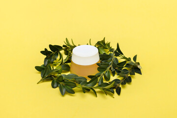 jar of cream with green leaf decor on a yellow background