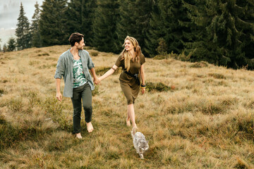 A beautiful couple in love are walking with the cat and smiling cheerfully in nature.