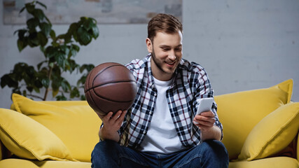 happy basketball fan holding ball and watching match on smartphone