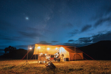 Tourists in yellow tent camping on hill with milky way in the night sky