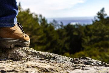 detail of a man's shoe perched on a rock in front of the green mountain landscape and the blue sky.