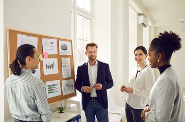 Wall Mural - Cheerful diverse office workers discuss financial risks and analyze charts and diagrams together. Positive colleagues discuss a new business project. Concept of planning, brainstorming and teamwork.