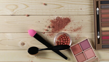 Makeup tools with beauty blender pile, brush set, eye shadow palette, nail file, tweezers and red lipstick wooden plank table surface, boards background and texture