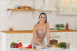 Smiling fitness woman in sportswear standing in kitchen and writing down healthy recipe or daily ration diet at home with fresh ingredients on table. Active healthy lifestyle, clean eating concept