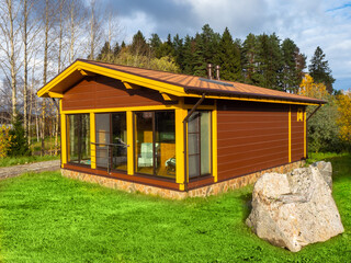 Wall Mural - One-story cottage with a beautiful sky and lawn. Private house on the background of an autumn forest. Panoramic Windows of cottages. House with a glazed veranda.